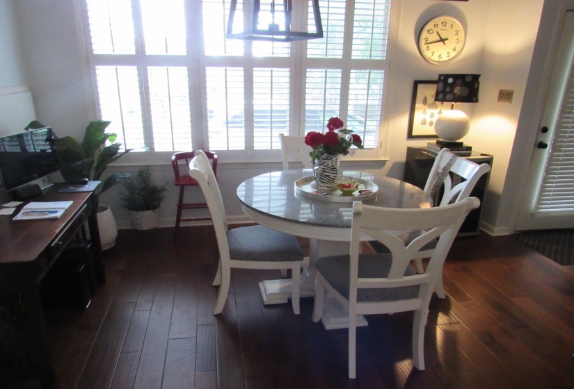 Dining area featuring wood-finish flooring, a round table with a stone-finish top, and window shutters