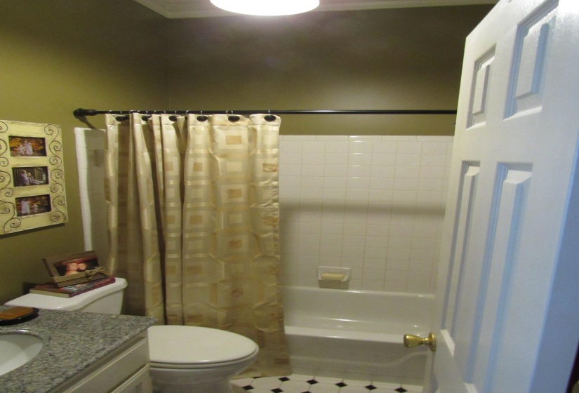 Bathroom featuring a bathtub with subway tile surround, a built-in toilet, and patterned black and white floor tiles