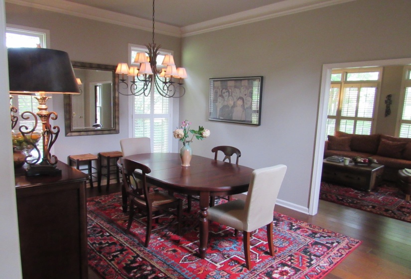 Formal dining room featuring crown molding, hardwood flooring, a multi-arm chandelier, and plantation shutters