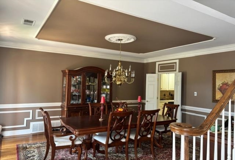 Dining area featuring wood finished floors, a chandelier, a tray ceiling, wainscoting, and crown molding