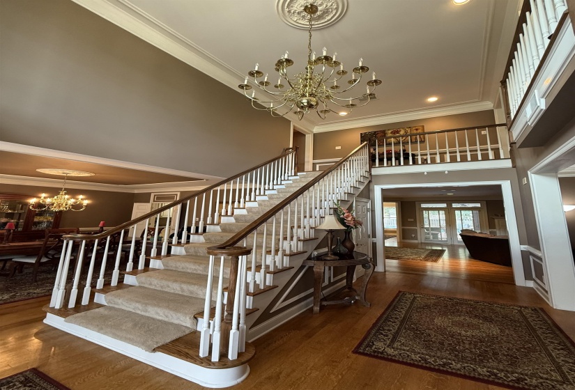 Stairway with a chandelier, ornamental molding, wood finished floors, a high ceiling, and recessed lighting