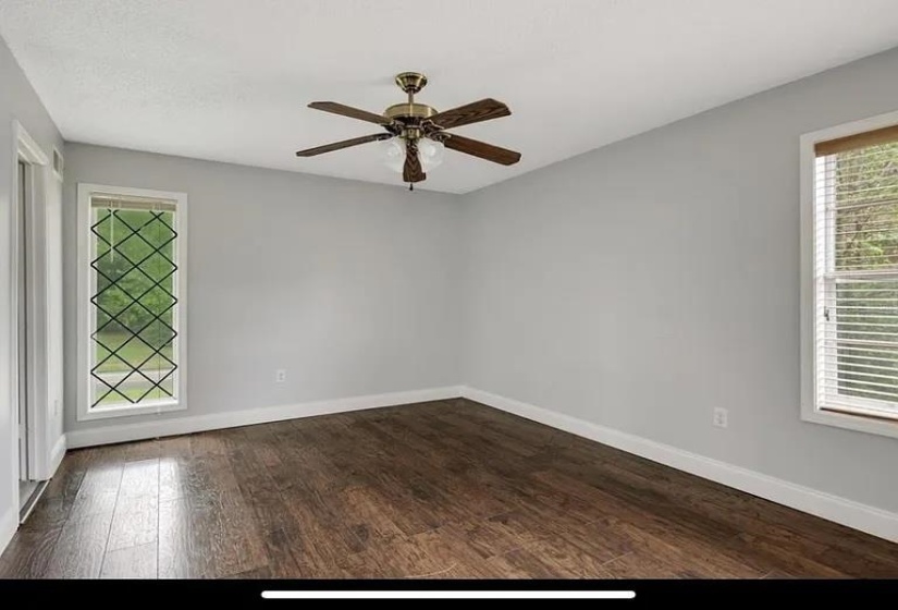 Room featuring wood-finish flooring, light gray walls, white trim, and a ceiling fan with integrated lighting