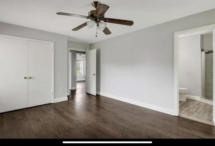 Spacious room featuring rich wood-finish flooring, light gray walls, a ceiling fan with integrated lighting, and white bi-fold closet doors