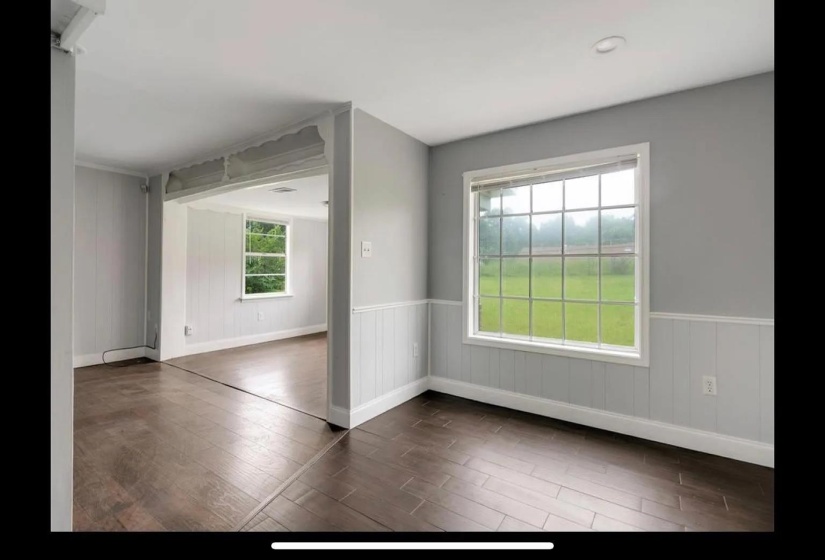 Interior space featuring wood-finish flooring, light grey walls with white wainscoting, and an expansive window overlooking a green exterior