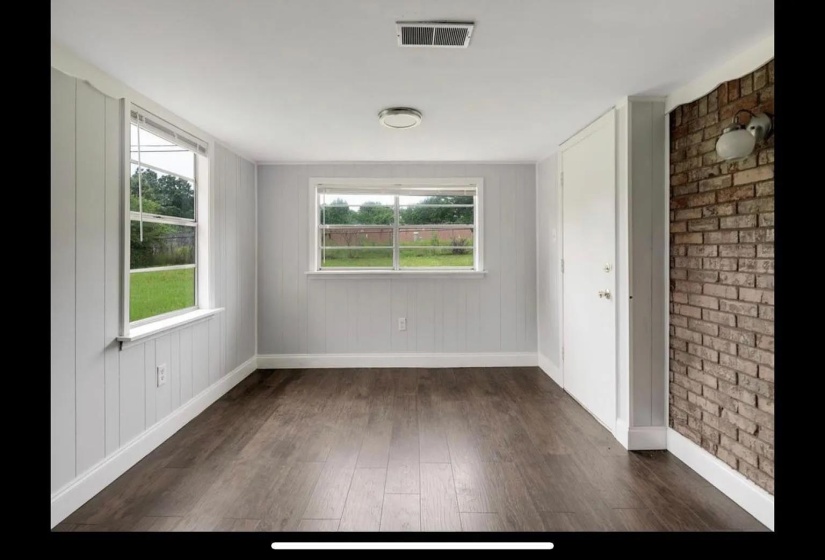 Spacious room featuring wood-finish flooring, two windows, and a brick accent wall