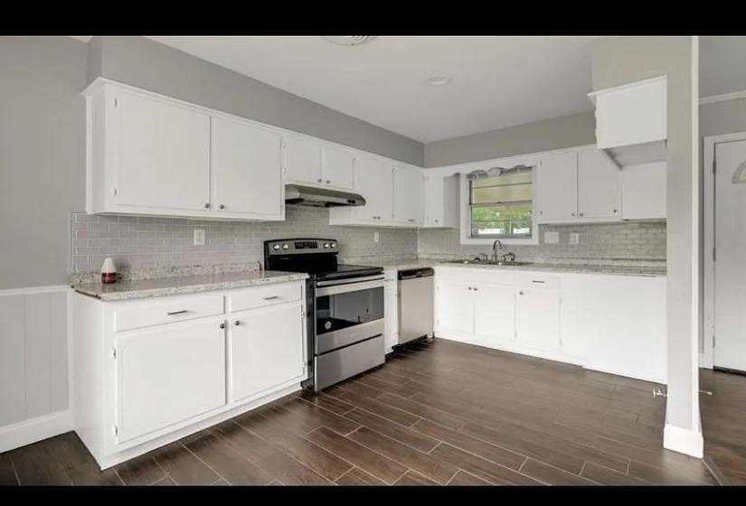 Kitchen featuring white cabinetry, light-toned countertops, a subway tile backsplash, stainless steel appliances, and wood-finish flooring