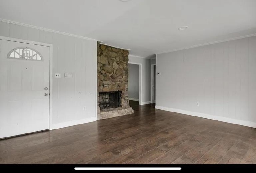 Living space featuring a stone-clad fireplace, wood-finish flooring, white paneled walls, and a recessed ceiling light