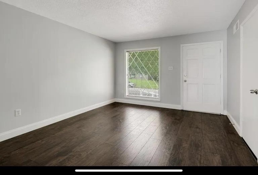 Spacious room featuring dark wood-finish flooring, light grey walls, and white trim