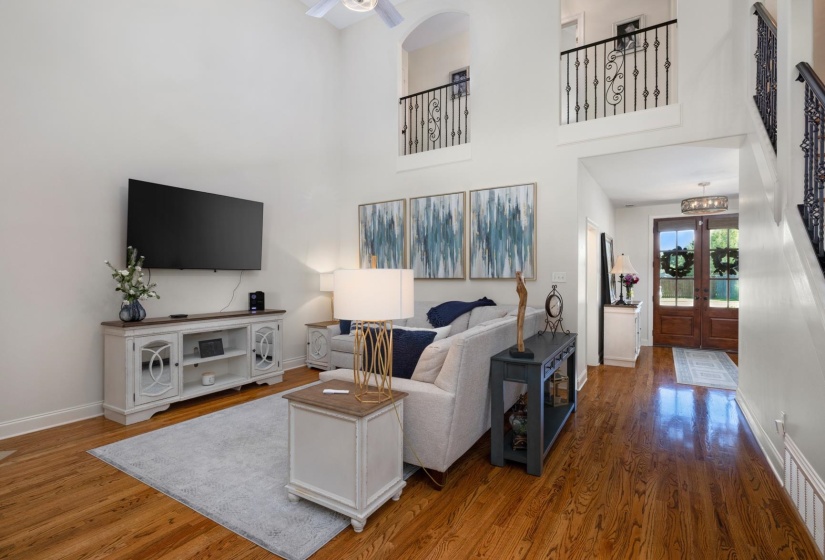 Two-story living area featuring wood-finish flooring, a vaulted ceiling, and an open upper landing with wrought iron railings