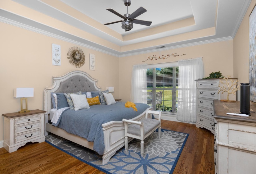 Hardwood flooring throughout this room features a tray ceiling with crown molding and a ceiling fan