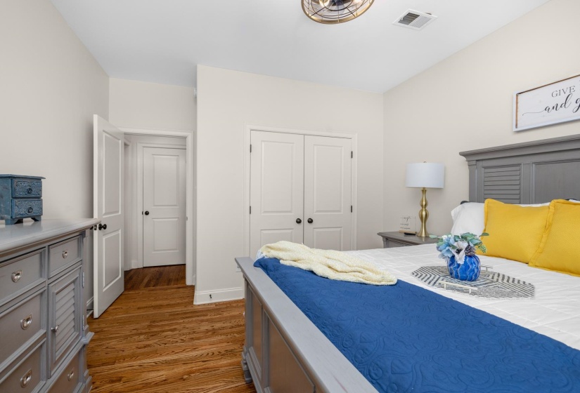 Warm wood-finish flooring complements light-colored walls in this room featuring recessed doors, a semi-flush mount ceiling fan, and a built-in closet with double doors