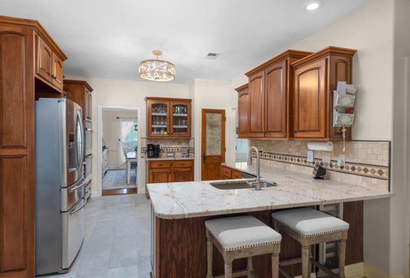 Spacious kitchen featuring warm wood cabinetry, light-toned granite countertops, a stainless steel French door refrigerator, and a coordinating tile backsplash with a decorative border