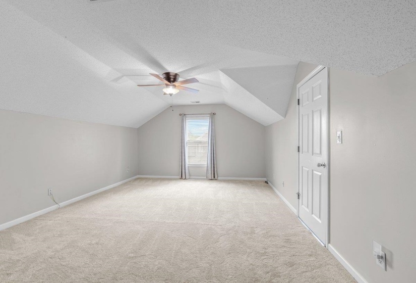 Carpeted room featuring a sloped ceiling, ceiling fan with integrated lighting, and a single window with curtains