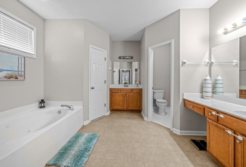 Bathroom featuring a built-in jetted tub, dual vanity with wood cabinetry, and a separate water closet