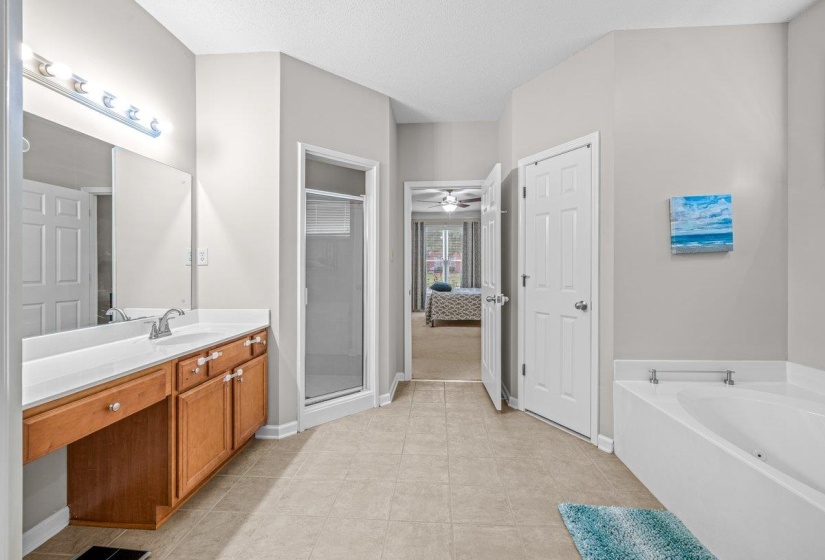 Spacious bathroom featuring a double vanity with wood-finish cabinetry, a large frameless mirror, a glass-enclosed shower, and a white soaking tub