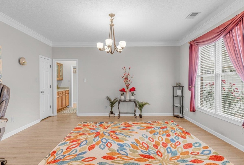 Spacious room featuring light wood-finish flooring, crown molding, and a five-light chandelier