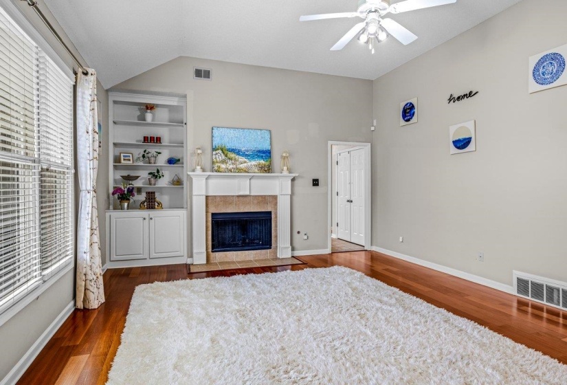 Spacious living area featuring a fireplace with a white mantel and tiled surround, built-in shelving, wood-finish flooring, and a ceiling fan