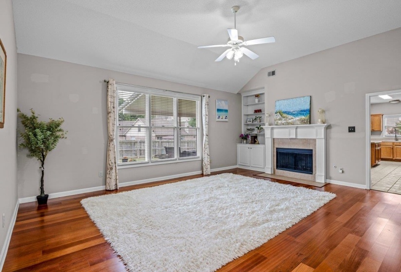 Spacious living area featuring high vaulted ceilings, rich wood-finish flooring, and a fireplace with a mantel and built-in shelving