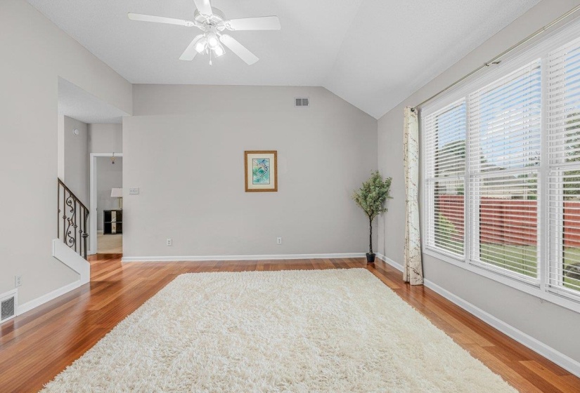 Living area featuring vaulted ceilings, wood-finish flooring, a ceiling fan, and large windows with horizontal blinds