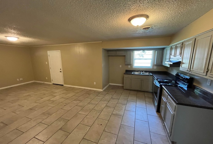 Kitchen and living area featuring tile flooring, light grey cabinetry, black countertops, and a full suite of black kitchen appliances