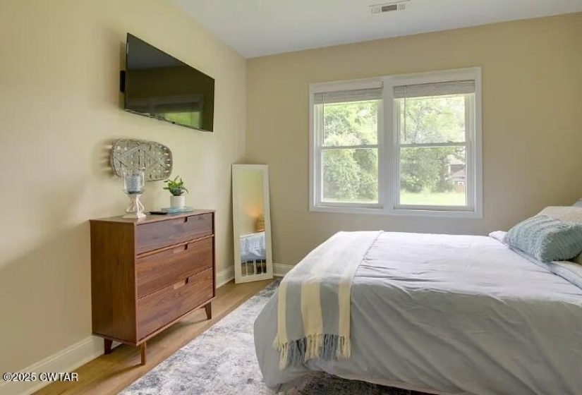 Bedroom featuring light neutral wall color, wood-finish flooring, and a double window