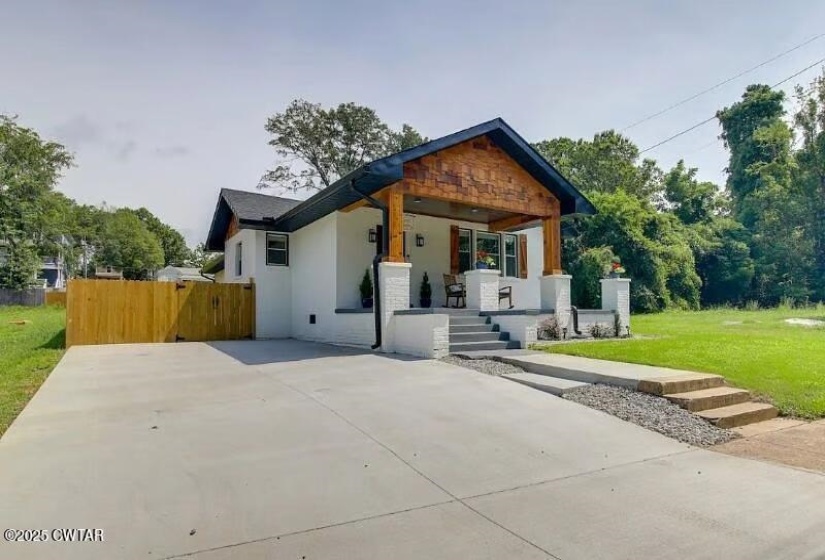 Contemporary bungalow featuring a covered front porch with wood-finish accents, white brick columns, and dark window shutters