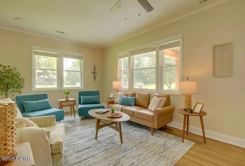 Spacious living area featuring ample natural light, light wood-finish flooring, a ceiling fan, and crown molding