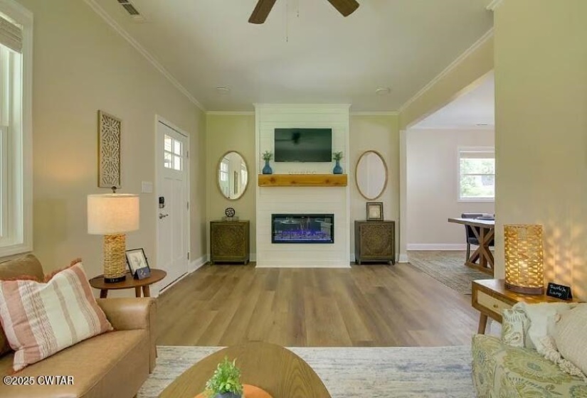 Living area featuring a white fireplace with a wood mantel, wood-finish flooring, and white trim