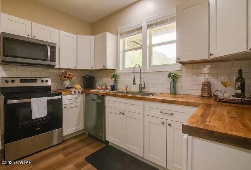 Kitchen featuring white shaker cabinetry, butcher block countertops, subway tile backsplash, stainless steel appliances, and wood-finish flooring