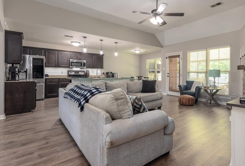 Open-concept living space featuring wood-finish flooring, a vaulted ceiling, and dark wood cabinetry in the kitchen