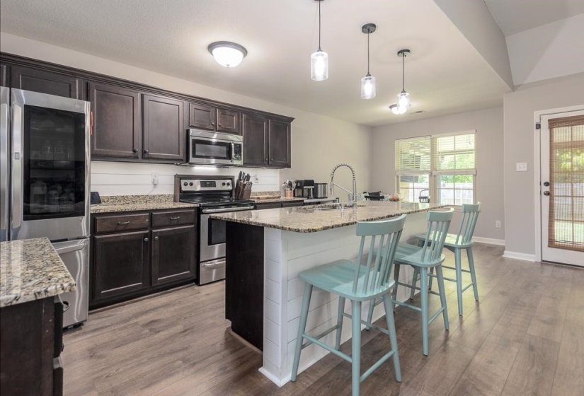 Kitchen featuring dark wood cabinetry, stainless steel appliances, a center island with granite countertop and pendant lighting, and wood-finish flooring
