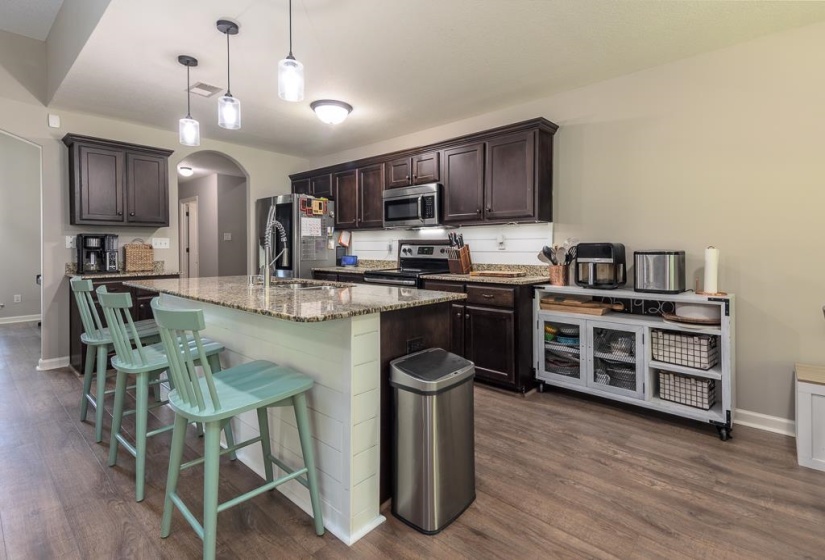 Kitchen featuring wood-finish flooring, dark wood cabinetry, granite countertops, and a full suite of stainless steel appliances