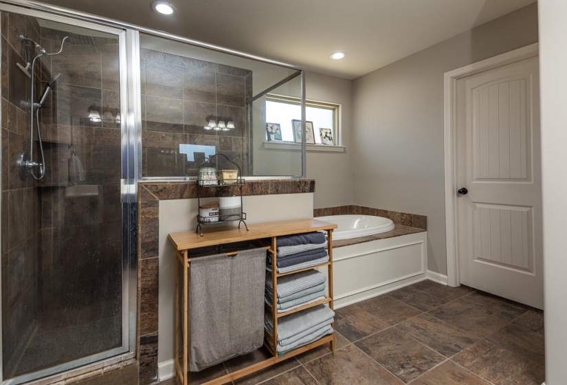 Bathroom featuring a glass-enclosed shower with dark-toned tile surround, a built-in soaking tub with a stone-finish deck, and large format floor tiling