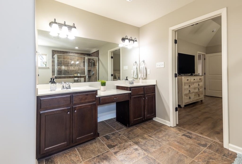 Bathroom featuring a dual vanity, integrated makeup counter, and a glass-enclosed shower with tiled walls