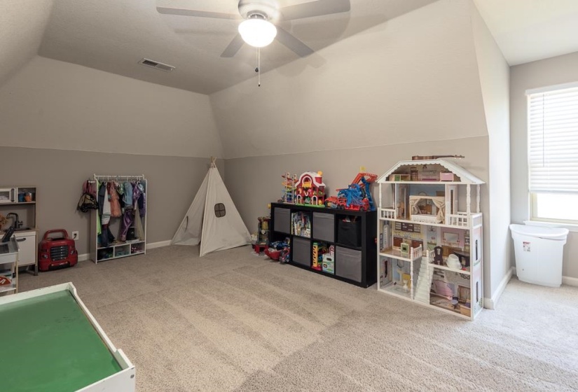 Spacious carpeted room featuring a ceiling fan, a window with blinds, and sloped ceiling details