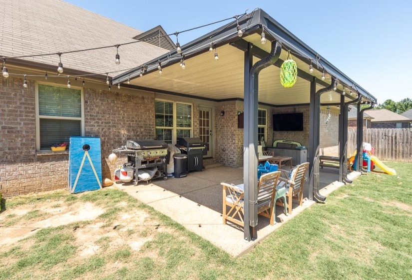 Expansive covered patio featuring a mounted television, string lighting, and direct access to the interior