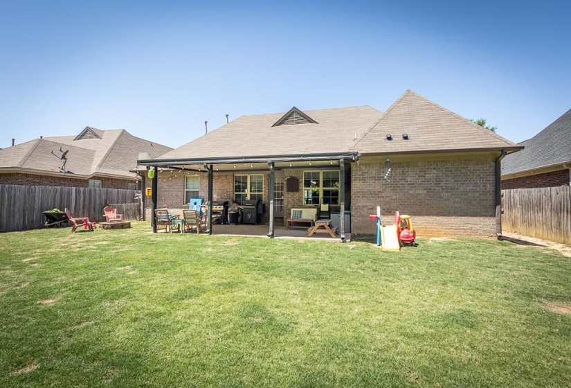 Expansive green lawn with a covered patio, brick exterior, and full privacy fencing