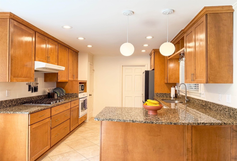 Kitchen featuring abundant wood cabinetry, granite countertops, tile flooring, recessed lighting, and a kitchen island with pendant lighting