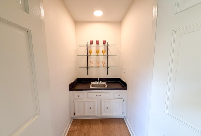Built-in wet bar featuring white cabinetry, a dark countertop, an undermount sink, and glass shelving
