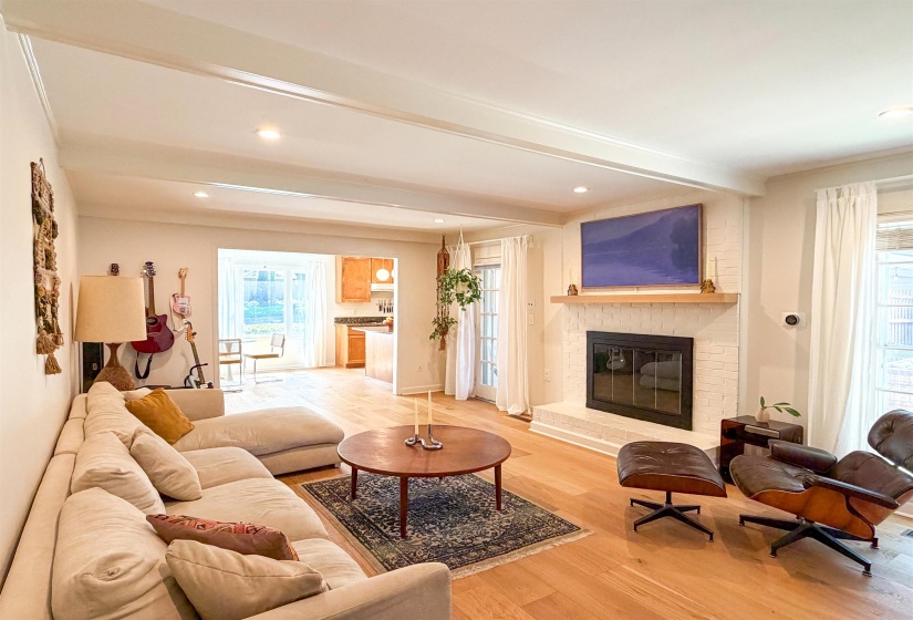Living area featuring a white painted brick fireplace with a wood mantel, light wood-finish flooring, recessed lighting, and a broad cased opening to a kitchen space