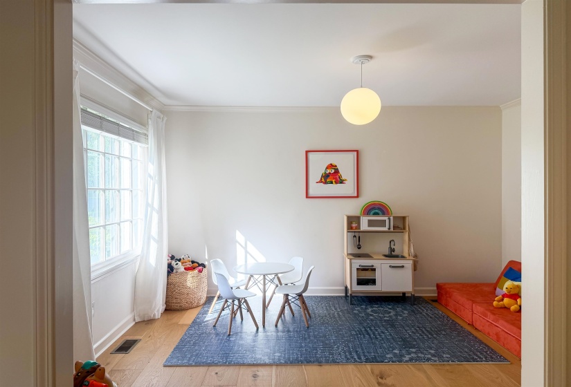Bright interior space featuring a multi-pane window, wood-finish flooring, a contemporary spherical ceiling light fixture, crown molding, and neutral wall tones
