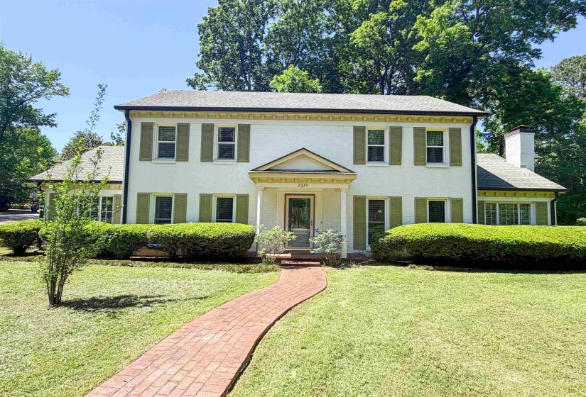 Traditional two-story residence featuring a brick facade, green shutters, and a prominent front entrance with a portico