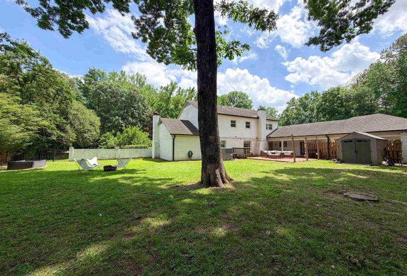 Spacious backyard featuring a manicured lawn, established perimeter trees, a multi-level deck, and a white painted brick exterior