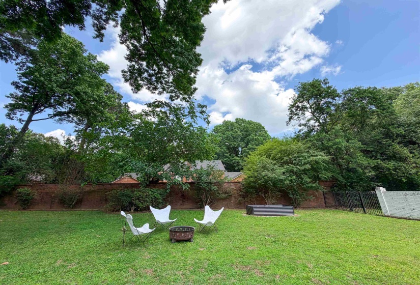 Spacious backyard featuring a lush green lawn, mature trees, and a brick privacy wall