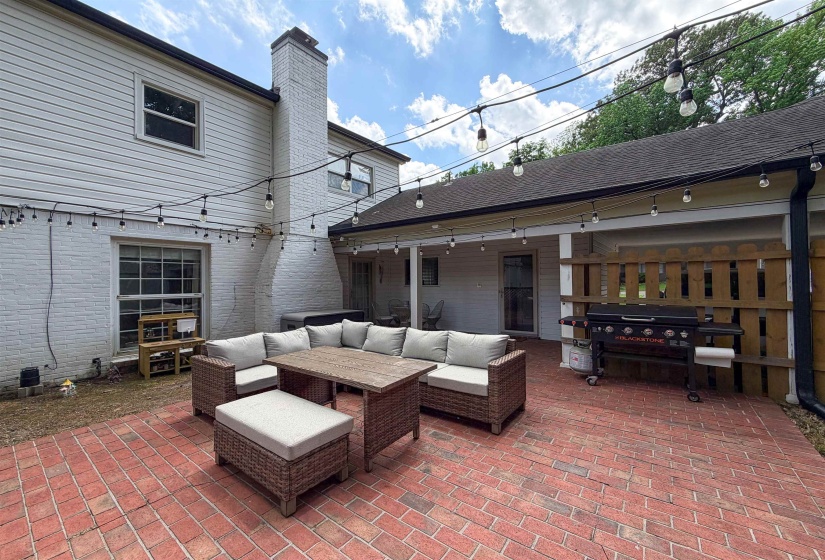 Brick paver patio with covered porch, white brick exterior, and a wood privacy fence