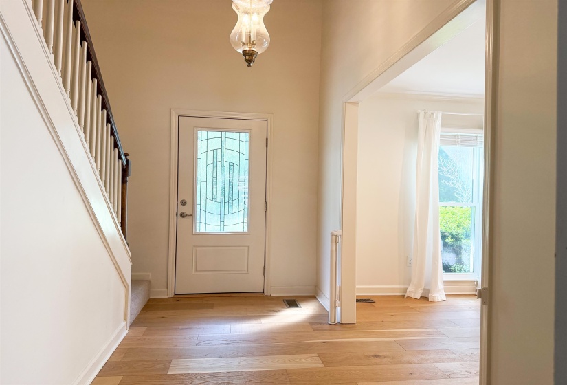 Entryway featuring a decorative glass front door, wood-finish flooring, a classic glass pendant light fixture, and a staircase with a white balustrade and dark wood handrail