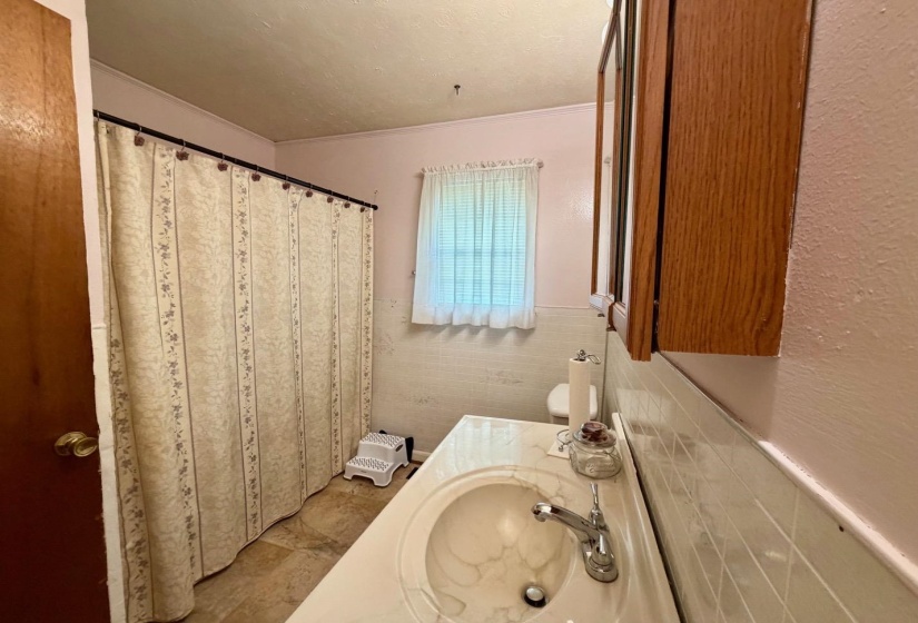 Bathroom vanity with integrated sink, chrome faucet, wood-finish medicine cabinet, and tiled walls