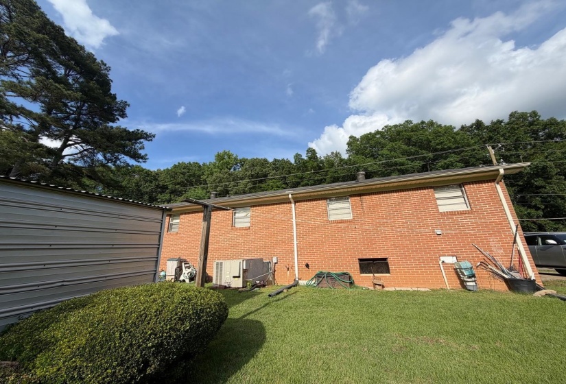 Brick exterior featuring multiple windows and a mature tree line backdrop