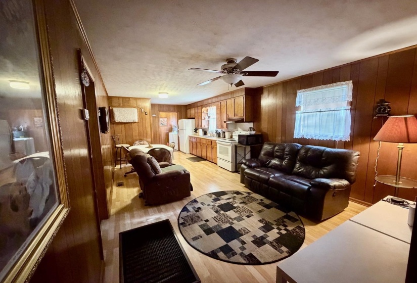 Open-concept living space featuring wood-finish paneling, light wood-finish flooring, and a ceiling fan with integrated lighting