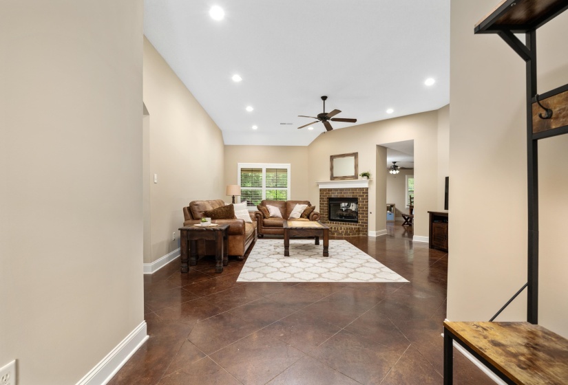 Spacious living area featuring vaulted ceilings, recessed lighting, and a brick fireplace with a mantel